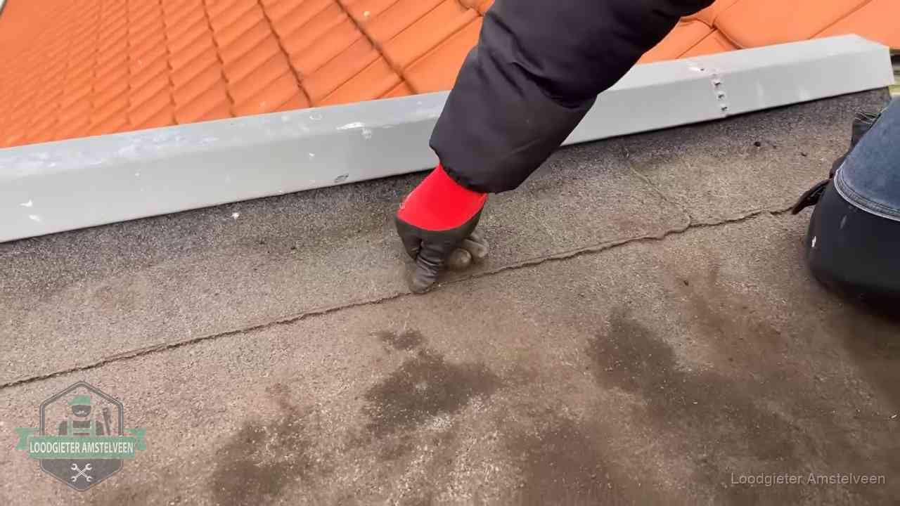 Vakman wijst een naad met vochtplekken aan op een bitumen plat dak in Amstelveen