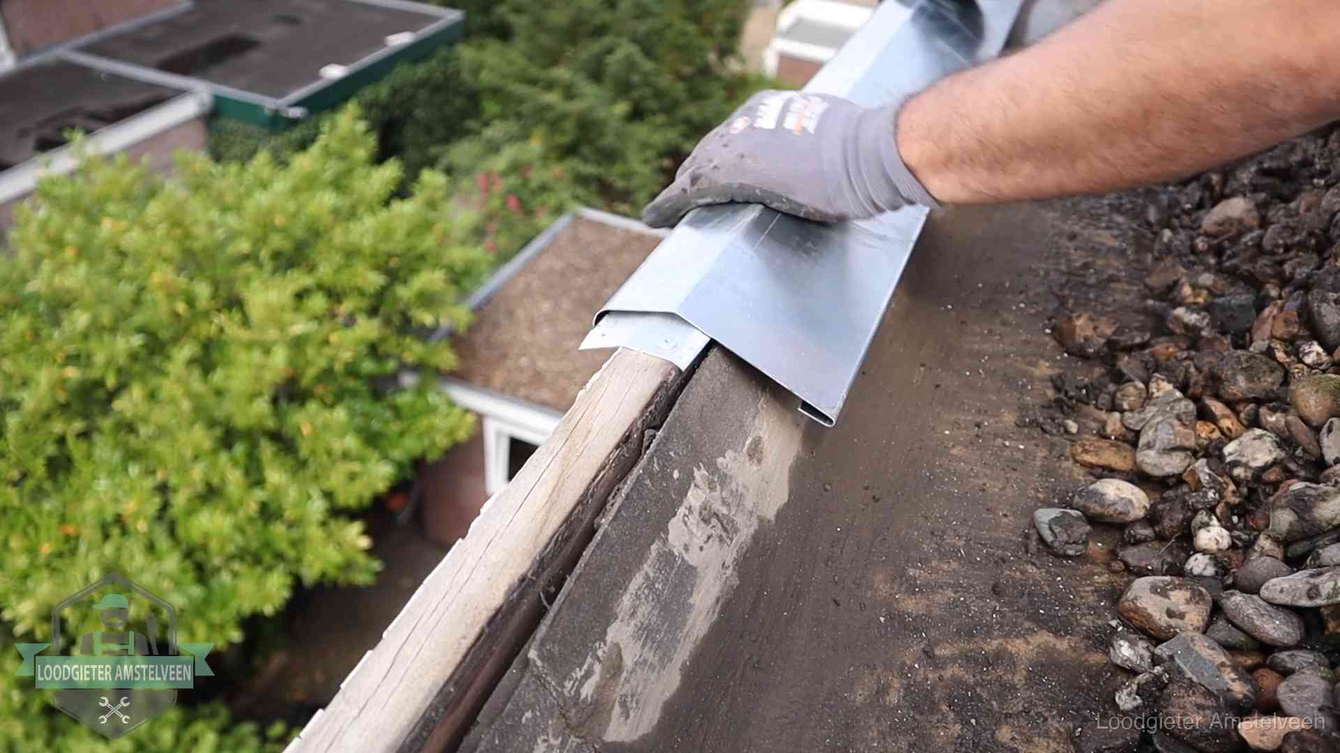 Dakdekker plaatst een zinken deklijst op een dakrand met uitzicht over een woonwijk in Amstelveen