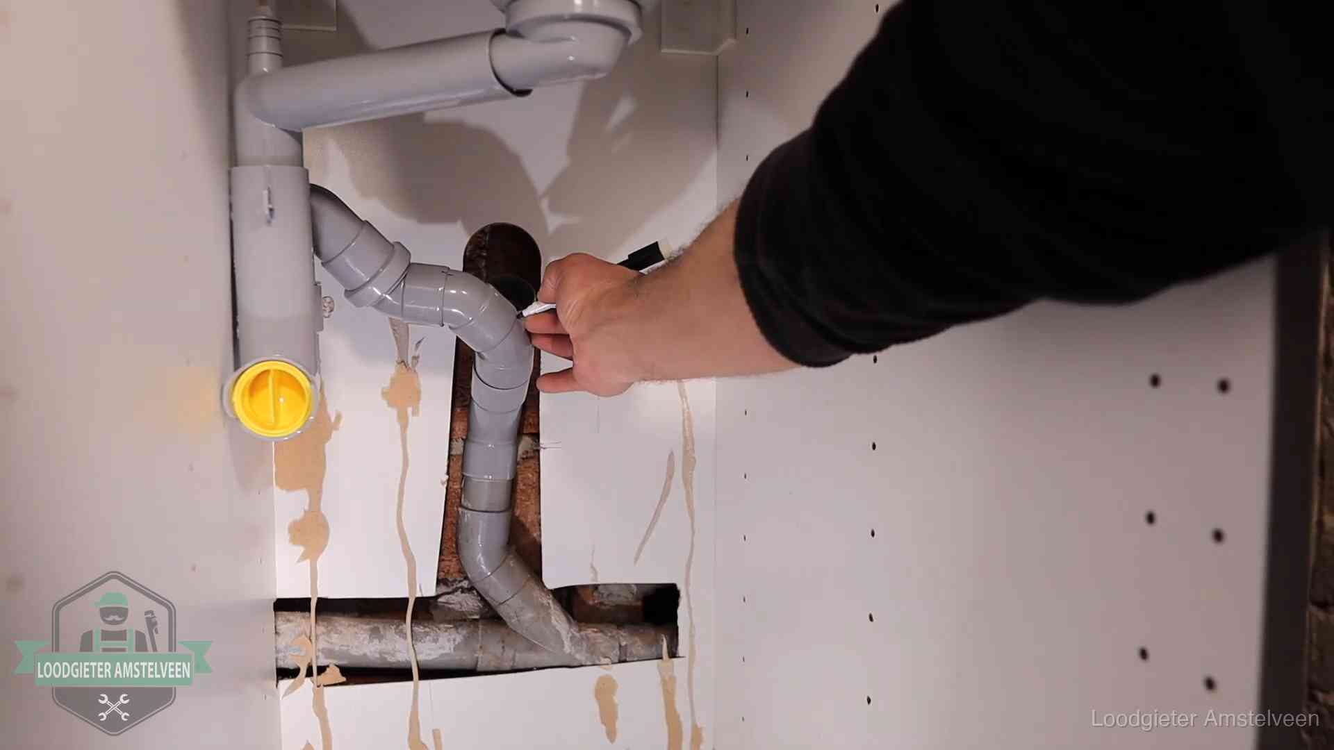 Loodgieter voor verhuurders en bedrijven in Amstelveen Loodgieter markeert een pvc-afvoerbuis onder een gootsteen in Amstelveen