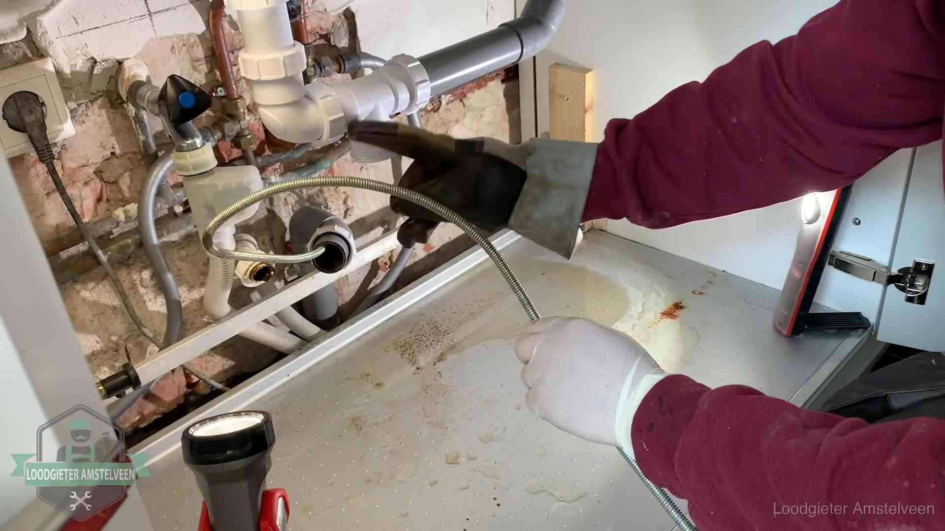 Ontstoppingsveer gaat in een geopende sifonaansluiting onder het aanrecht in Amstelveen