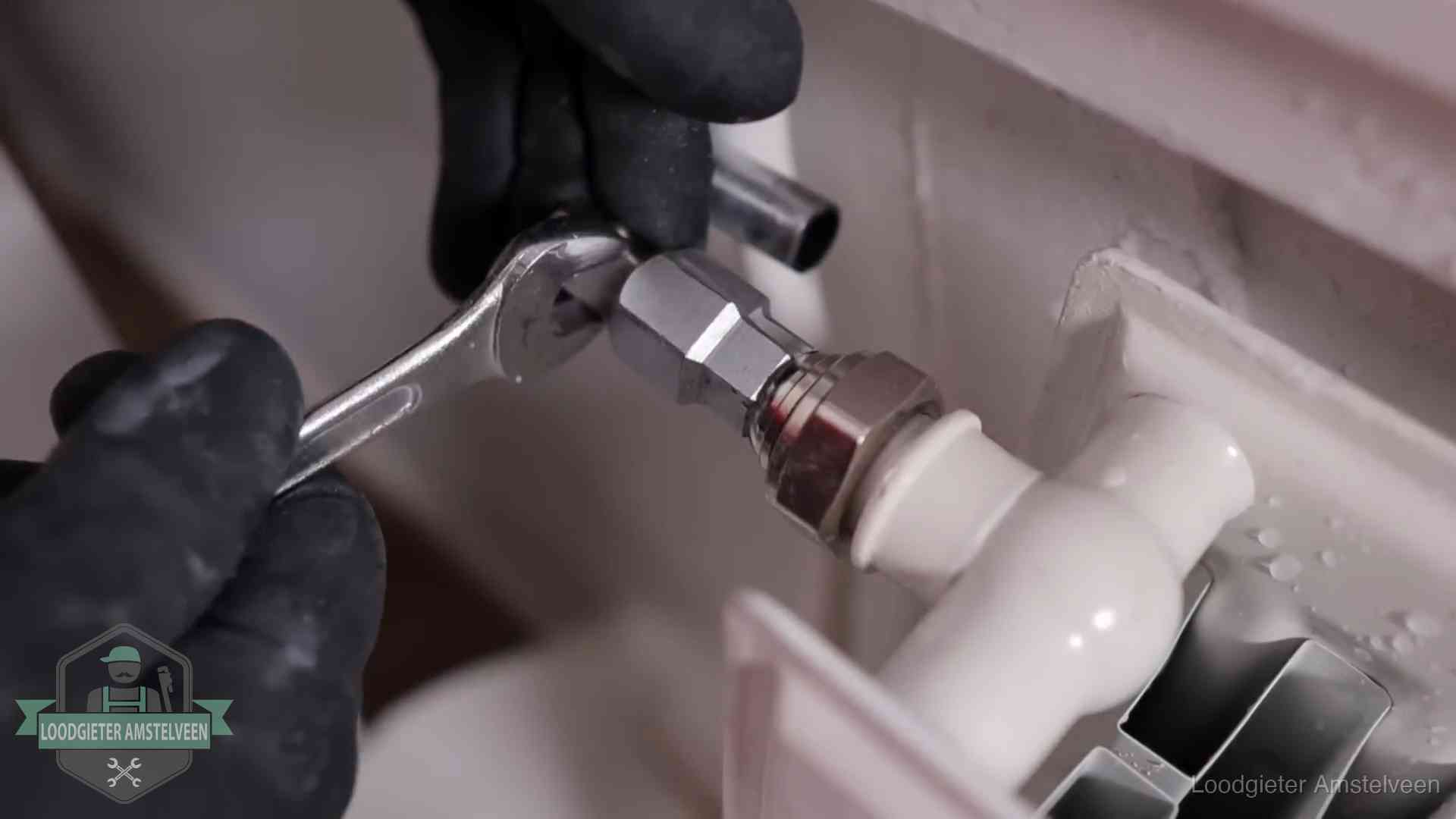 Steeksleutel draait een wartelkoppeling op een radiatorkraan aan in Amstelveen