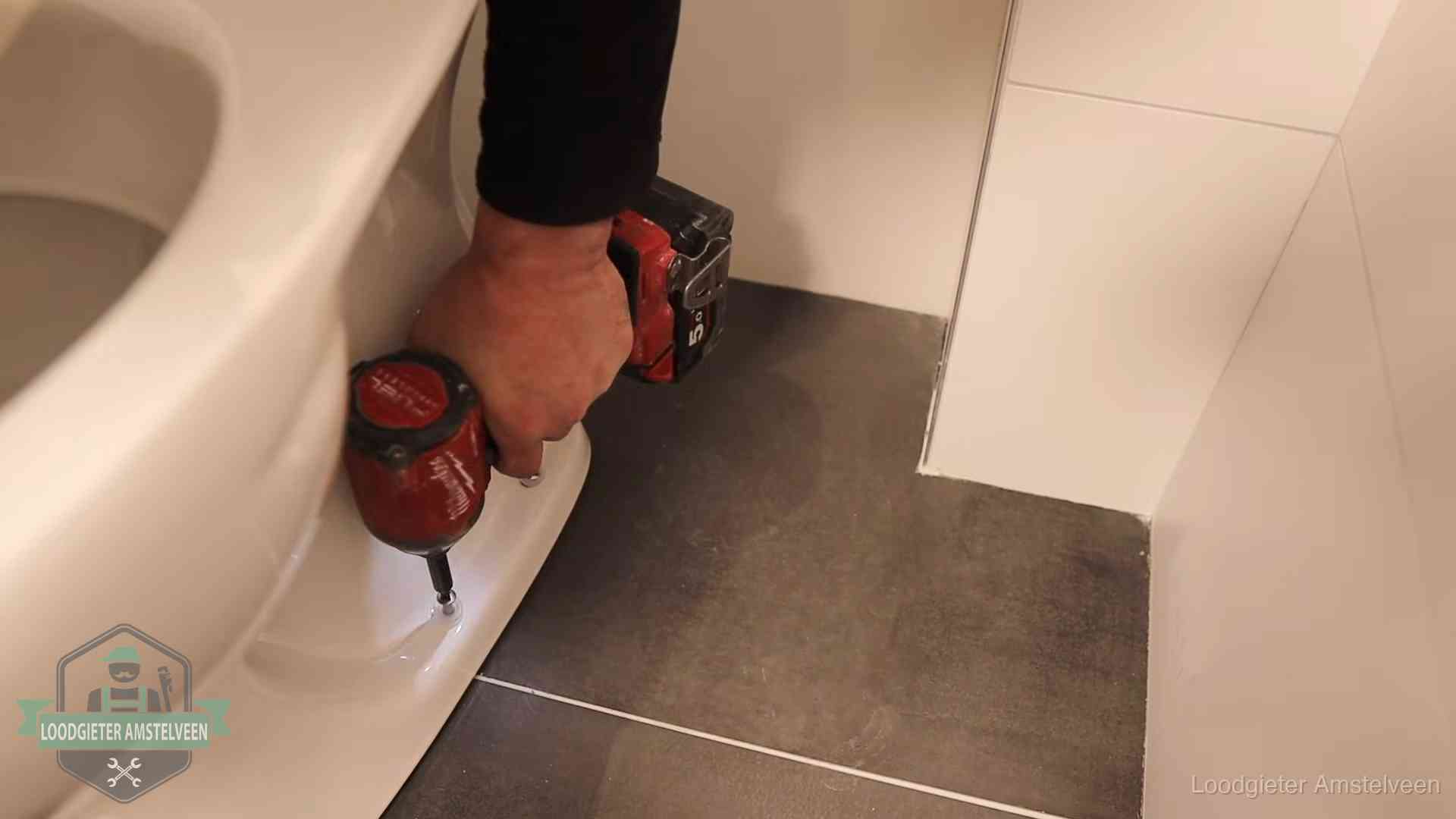 Kosten wc ontstoppen in Amstelveen Loodgieter zet de voet van een wc-pot vast op de tegelvloer in Amstelveen